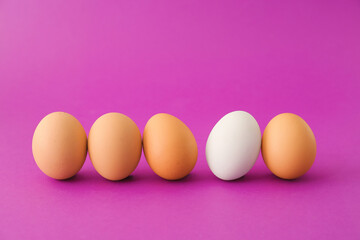 White egg among brown ones on color background. Concept of uniqueness