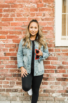 Woman in denim jacket leaning against red brick wall