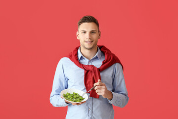 Handsome young man with plate of tasty ravioli on color background