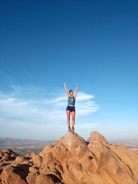 Woman on standing and raising her on top of mountain under blue sky
