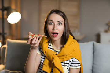 Beautiful young woman eating tasty pizza while watching TV at home in evening