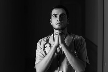 Black and white portrait of praying male doctor on dark background