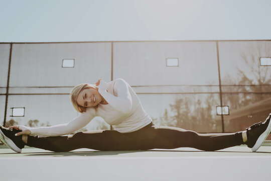 Woman stretching her legs near a fence outdoor during daytime