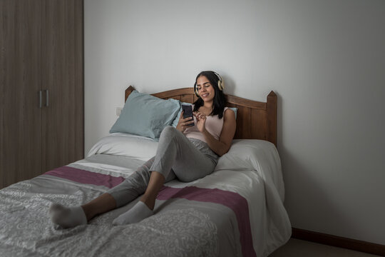 Woman wearing headset and using smartphone in bed