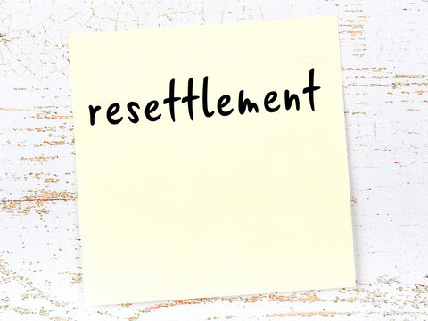 Yellow sticky note on wooden wall with handwritten word resettlement