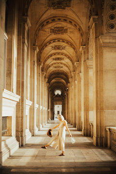 Woman wearing jumpsuit and holding a hat standing in hallway at Cafe' Marly in Paris, France