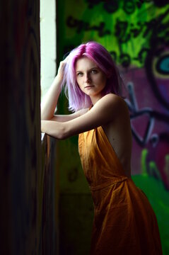 Woman with pink hair in yellow dress leaning on window