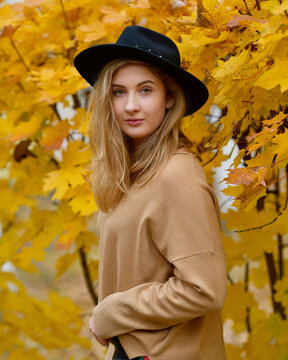 Young woman with a black hat standing beside yellow tree leave