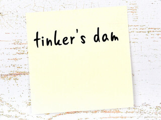 Yellow sheet of paper with word tinker's dam. Reminder concept - obrazy, fototapety, plakaty