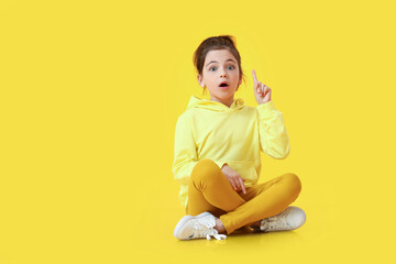 Cute little girl with raised index finger on color background