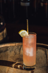 pink lemonade cocktail with lemon wedge and gold drinking straw atop whiskey barrel 