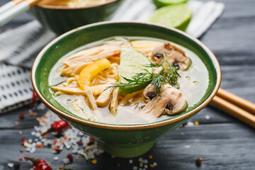 Bowl of tasty Thai soup with chicken on dark wooden background