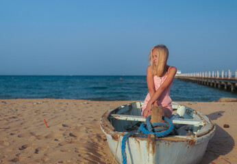 teenage girl with blonde hair sit on an old boat to the shore of the sea.