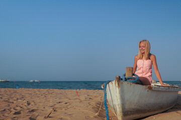 teenage girl with blonde hair sit on an old boat to the shore of the sea.