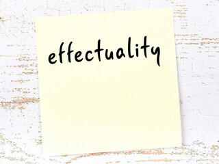 Yellow sticky note on wooden wall with handwritten word effectuality