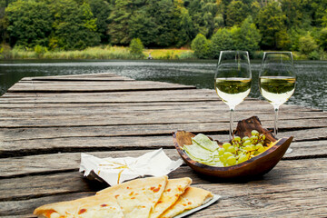 Picnic at the wooden pier by the lake with food, fruit and white wine. Picnic for two, romantic outdoor recreation