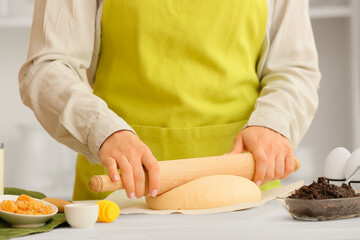Woman preparing tasty poppy seed bun at table in kitchen, closeup