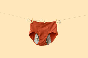 Period panties hanging on rope against color background