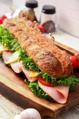 Board with tasty ciabatta sandwich on light wooden background, closeup