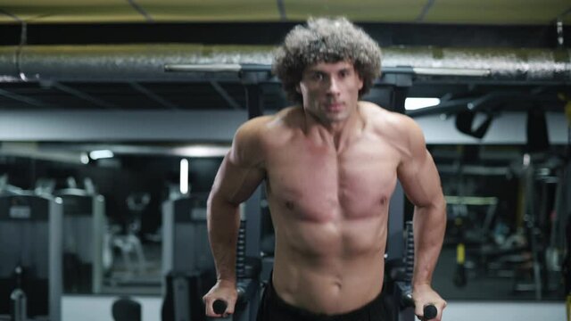 Man exercising on parallel bars. Young athlete exercising in gym. Steadicam shot zoom out.