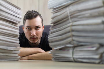Close up portrait of a young journalist and a stacks of newspapers in blurred foreground