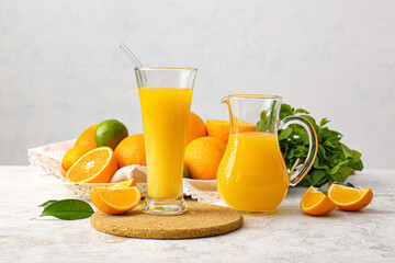 Jug and glass of tasty orange juice on light background