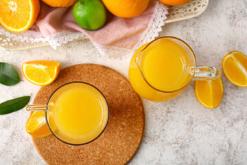 Jug and glass of tasty orange juice on light background