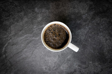 Fresh cup of black coffee with bubbles on dark background
