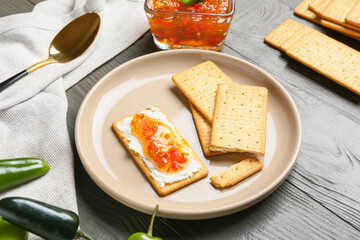Delicious crackers with cottage cheese and jalapeno pepper jam in plate on grey wooden table