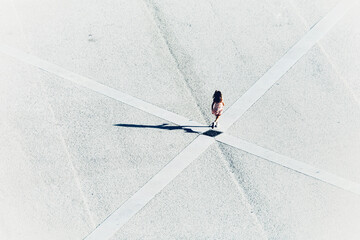 Top view of a girl in flower dress running across the diagonal of a monochrome deserted square