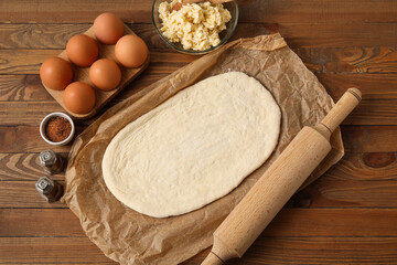 Fresh dough and ingredients for khachapuri on wooden background