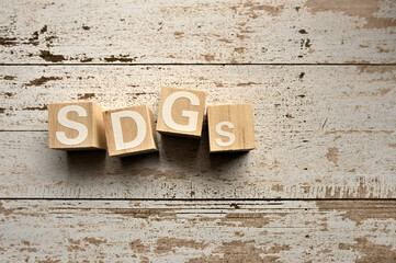 On a white damaged wood board, wooden word cubes are arranged in the letters SDGs. It is an abbreviation for Sustainable Development Goals.