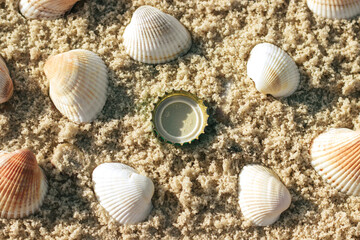 The concept of pollution of the planet, the bottle cap lies among the shells on the sand, layout, top view