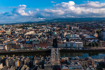 Naklejka premium Aerial view of skyline of Dublin with river flowing with cars running on bridge connecting two sides of street surrounded by buildings during a cloudy day