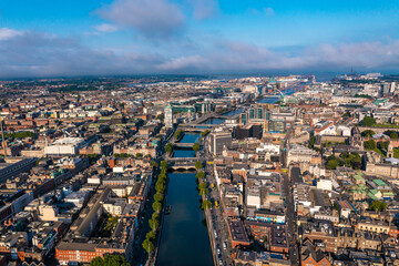 Fototapeta premium Establisher shot of Dublin skyline with river flowing with bridge connecting two sides of street surrounded by buildings during a cloudy day