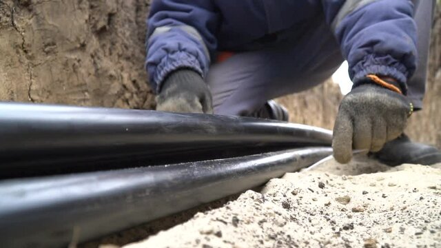 Close up footage of a worker using zip ties on three thick cables in a trench