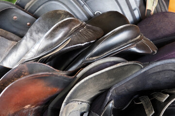 Horse equipment. Many leather horse saddles as background. Old saddle, saddler