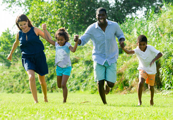 Friendly interracial family with two children having fun together, running in summer city park