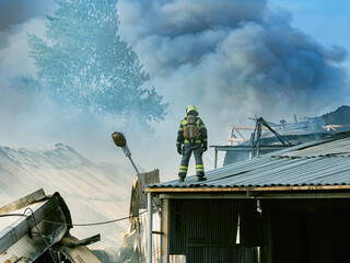 Fireman inspects fire consequences. Rescuer stands on the roof of the house. Black smoke from fire....