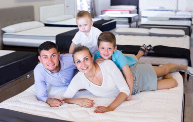 Young family with children are testing quality of mattress in store.