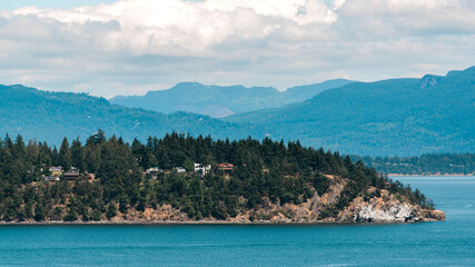 Fototapeta premium Forested island in the bay with mountains in the background.