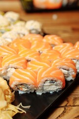 Hand Waiter holding Set Delicious fresh Sushi slate plate, Japanese raw fish in traditional restaurant. Philadelphia fresh Rolls served on plate in sushi bar. waiter in gloves holds sushi rolls