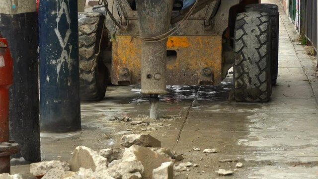 close-up of a skid steer loader with hydraulic hammer breaking and demolishing concrete from the sidewalk in the daytime in 4k