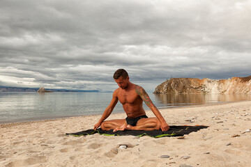 Fototapeta na wymiar strong young man does yoga on the sandy shore of a mountain lake, yoga practice on the beach