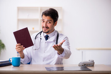 Young male doctor reading book in the clinic