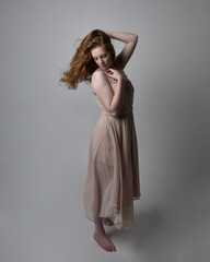 Full length portrait of pretty red haired woman dancer,  wearing skin toned flowing fairy dress. Standing gestural poses  isolated on studio background.