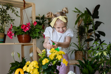 a little blonde girl with a headband on her head and wearing work gloves sprays from a bullet dispenser or waters indoor flowers. Home gardening, caring houseplants. Space for text. High quality photo