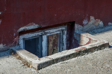 An old window in the basement. Part of a dilapidated 19th century building, painted with red paint. Living conditions in the old town.