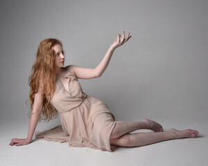 Naklejka premium Full length portrait of pretty red haired woman dancer, wearing skin toned flowing fairy dress. Sitting gestural poses isolated on studio background.