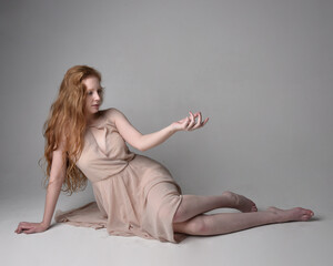 Naklejka premium Full length portrait of pretty red haired woman dancer, wearing skin toned flowing fairy dress. Sitting gestural poses isolated on studio background.